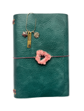 Green leather journal with a pink druzy geode talisman on the front and a gold bookmark featuring three charms: a star-shaped strawberry quartz, a “SPIRITUAL BADDIE” tag, and a round 222 charm.