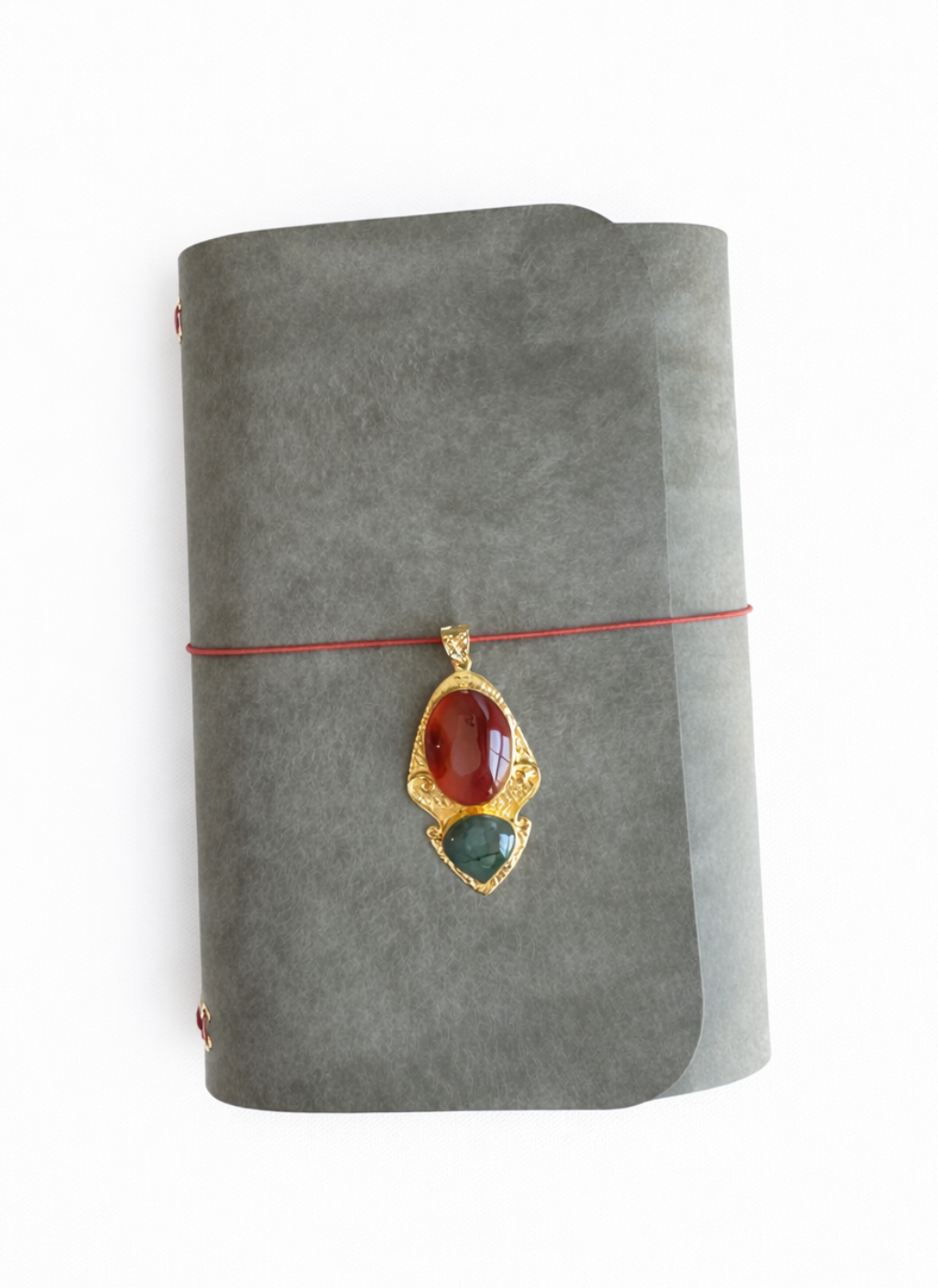 Veg tan leather grey with olive tone Pueblo finish tri fold journal with a gold pendant featuring red and green stones on a white background